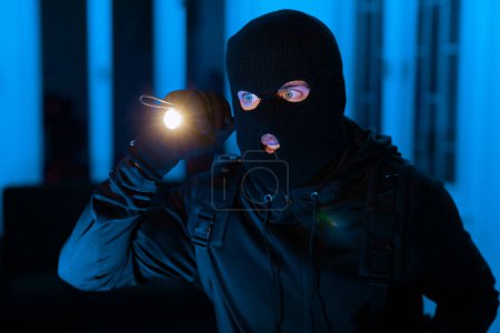 Esta imagen captura a un ladrón en el acto con una linterna, en busca de objetos de valor para robar en un apartamento durante la quietud de la noche