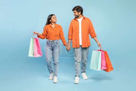 Lächelndes indisches Paar hält Händchen und trägt bunte Einkaufstüten, was auf ein angenehmes Einkaufserlebnis hindeutet