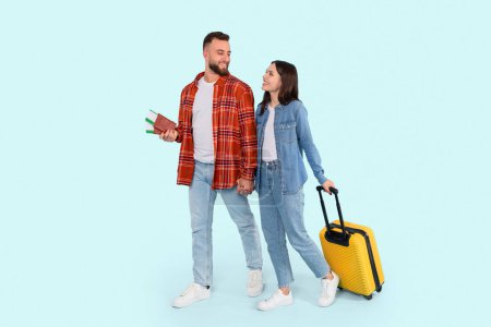 Téléchargez les photos : Cette photo représente un couple heureux de zoomeurs préparé pour le voyage, avec l'homme tenant des passeports et la femme avec une valise, tous deux isolés sur un fond de sarcelle - en image libre de droit
