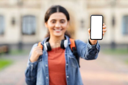 Téléchargez les photos : Jeune femme indienne sur le campus universitaire offrant un écran flou smartphone, capturant la technologie et l'éducation dans la vie moderne - en image libre de droit