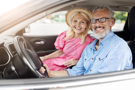 Téléchargez les photos : Joyeux couple retraité profitant d'une promenade en voiture, la femme portant un chapeau, la fenêtre vers le bas, représentant la liberté et la joie - en image libre de droit