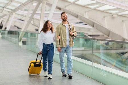 Foto de Un alegre hombre y una mujer caminan a través de un aeropuerto, el hombre con pasaportes y tarjetas de embarque, pareja disfrutando viajando juntos - Imagen libre de derechos