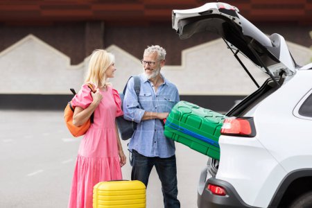 Téléchargez les photos : Un couple marié âgé organise ses valises colorées dans le coffre de sa voiture, représentant les aspects actifs et préparés de la vie à la retraite - en image libre de droit