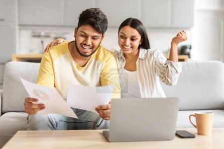 Ein fröhliches indisches Paar, das junge Millennials repräsentiert, genießt es, gemeinsam Finanzdokumente zu Hause zu analysieren, Laptop und Kaffee beiseite gelegt