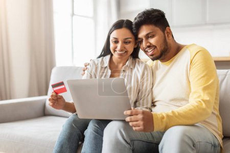 Foto de Una pareja india se ve enfocada en una computadora, probablemente comprando o navegando, con una tarjeta de crédito a mano, en un entorno hogareño - Imagen libre de derechos