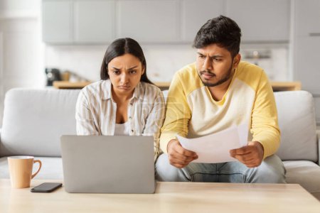 Ein besorgtes indisches Millennial-Paar scheint seine Hausfinanzen sorgfältig unter die Lupe zu nehmen, Dokumente und ein Laptop deuten auf ernsthafte Diskussionen hin.