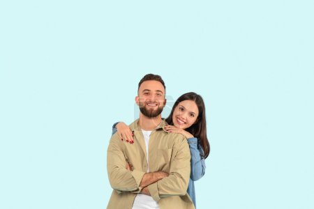 Téléchargez les photos : Homme et femme joyeux embrassant et souriant sur un fond bleu clair uni, tous deux vêtus avec désinvolture - en image libre de droit