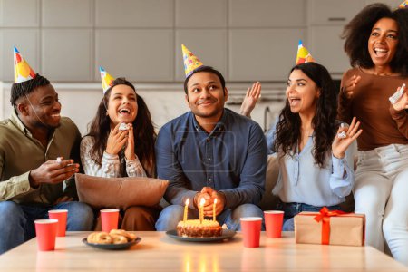 Foto de Jóvenes amigos multirraciales reaccionan con emoción y alegría mientras celebran un evento de cumpleaños juntos en casa - Imagen libre de derechos