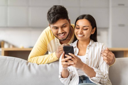 Téléchargez les photos : Un jeune couple indien joyeux intimement blotti devant un smartphone, partageant peut-être un moment de connexion numérique - en image libre de droit