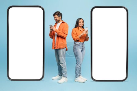 Photo for Two smartphones with blank screens flanking Indian man and woman focused on their phones, for mockups - Royalty Free Image