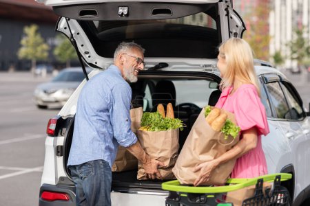 Ein Rentnerehepaar verstaut seine Einkaufstaschen im Kofferraum seines Autos und unterstreicht damit sein aktives, unabhängiges Leben