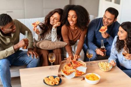 Foto de Los jóvenes multirraciales se ríen y disfrutan de una fiesta casual de pizza juntos, simbolizando amistad y comodidad en el hogar - Imagen libre de derechos