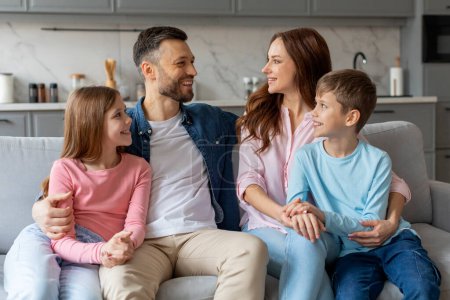 Photo for A cheerful family with two children sitting closely on a couch in a cozy living room, enjoying a pleasant moment together - Royalty Free Image