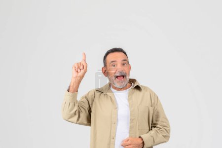 An old man shows excitement, pointing up enthusiastically, isolated on a neutral background, copy space