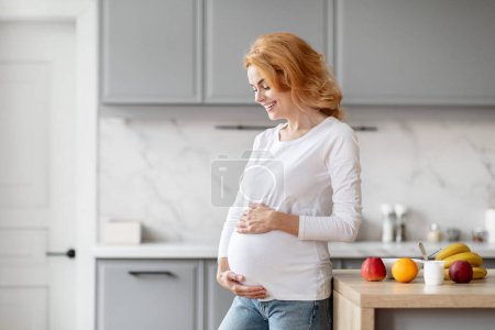 Europäische schwangere Frau in schicker Küche berührt ihren Bauch, symbolisiert Hoffnung und zukünftige Mutterschaft, Kopierraum