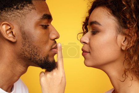 Photo for Hush. Profile of mysterious woman touching male lips with finger, orange studio background - Royalty Free Image