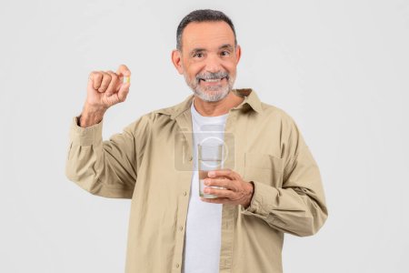 Senior man prepares to take medication, holding a pill and water, isolated on white studio background