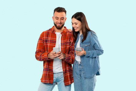 Dos estudiantes alegres, una pareja, están mirando a los teléfonos inteligentes, que representan el estilo de vida de la generación z de Zoomer, aislados sobre un fondo azul