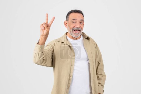 Smiling elderly man making a peace sign with his hand, isolated on a white background, conveys a laid-back and happy demeanor