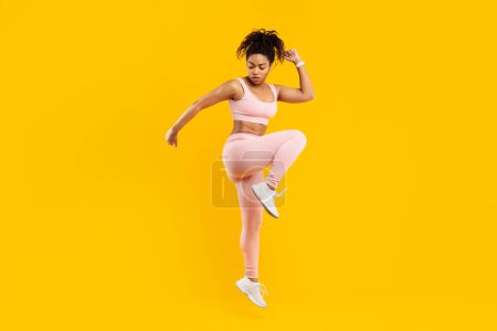 Photo for Vivid image of an african american lady in mid-air fitness routine, showcasing energy and liveliness, isolated against a yellow background - Royalty Free Image