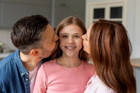 Foto de Una familia europea que expresa amor y afecto con los padres dando besos a su hija sonriente en casa - Imagen libre de derechos