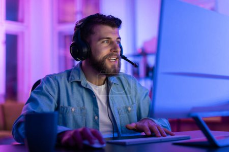 A bearded man wearing a gaming headset is focused on a screen in a neon-lit room, suggesting a gaming session