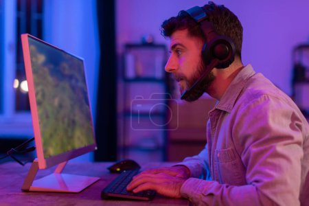 In a room lit by soft neon light, a guy gamer plays a first-person shooter game on their modern PC setup