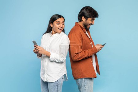 Indian couple focused on their smartphones, highlighting modern connectivity or social media, woman peeking on her man