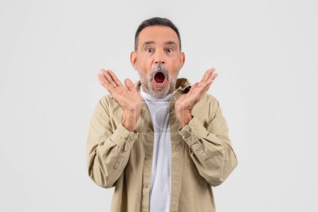 Shocked elderly man with raised hands and an open mouth expressing surprise, isolated on a white background