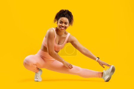 Photo for An african american woman performing a dynamic fitness side lunge, demonstrating agility and strength, isolated on a yellow backdrop - Royalty Free Image