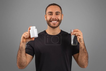 Ein fröhlicher Mann mit einer Flasche Pillen und einem Glas Wasser, der einen gesunden Lebensstil und Nahrungsergänzungsmittel fördert