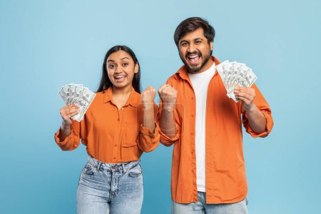 Indian man and woman excitedly holding and displaying cash, symbolizing financial success or win on blue