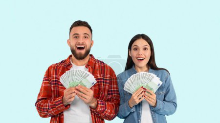 A young man and woman stand against a blue background, expressing surprise and happiness while holding a fan of cash