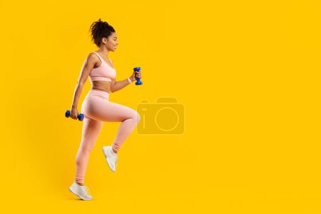 Photo for Determined african american lady engaged in a rigorous fitness routine with dumbbells, highlighting strength and focus, against an isolated yellow background - Royalty Free Image