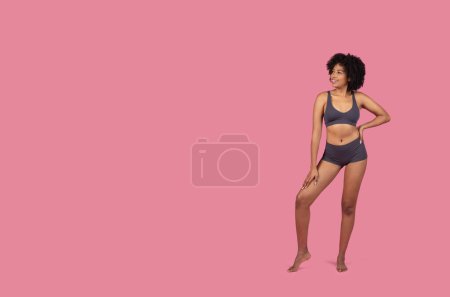 Téléchargez les photos : Une dame noire isolée se tient d'une main sur sa hanche, présentant un look sportif sur fond rose, indiquant une aura vive et positive - en image libre de droit