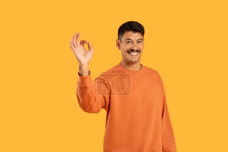 Millennial chico con un bigote haciendo un gesto de la mano OK divertido, exhibido sobre un animado fondo naranja aislado