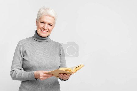 Photo for A delighted senior European woman immersed in reading a hardcover book, encapsulating a s3niorlife of learning - Royalty Free Image