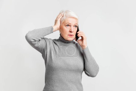 Photo for Elderly European woman senior appears puzzled during a phone call, depicting the varied experiences of s3niorlife technology interaction - Royalty Free Image