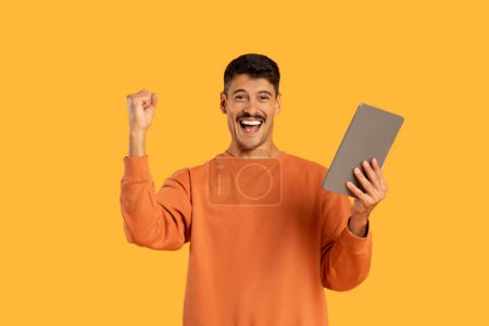 Photo for A funny millennial guy with a moustache isolated celebrates with a tablet, an image of joy and victory - Royalty Free Image