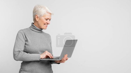 Fröhliche Seniorin, die mit dem Tippen auf einem Laptop beschäftigt ist, symbolisiert die Verschmelzung von Alter und digitalem Know-how, die von s3niorlife unterstützt wird