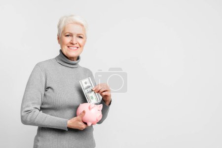 Téléchargez les photos : Femme européenne âgée optimiste avec une tirelire, illustrant la prudence financière et les habitudes d'épargne dans s3niorlife - en image libre de droit