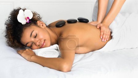 Téléchargez les photos : Massage de pierre. Esthéticienne professionnelle massant le dos féminin dans le salon de spa - en image libre de droit