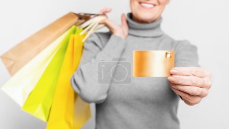 Foto de Una alegre mujer europea de alto nivel mostrando su tarjeta de crédito mientras sostiene coloridas bolsas de compras, encarnando la independencia financiera y s3niorlife - Imagen libre de derechos