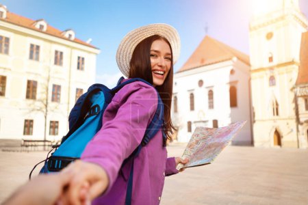 Photo for Young lady backpacker with a map pulling someone hand in an old European town, symbolizing adventure and discovery - Royalty Free Image