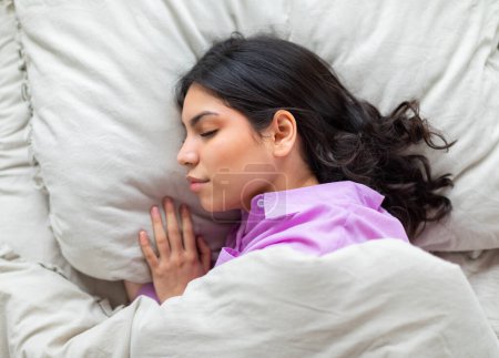 Téléchargez les photos : Jeune femme musulmane dort paisiblement au lit, incarnant la tranquillité et le confort à la maison, vue sur le dessus - en image libre de droit