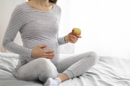 Foto de Esta imagen captura a una mujer embarazada en casa, haciendo una elección saludable durante su embarazo al comer una manzana - Imagen libre de derechos