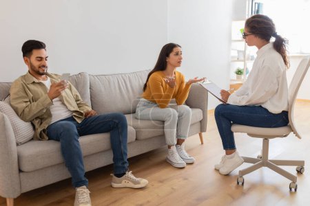 A young couple seems in a distraught state as they converse with a therapist during a potentially intense family session or marriage counseling