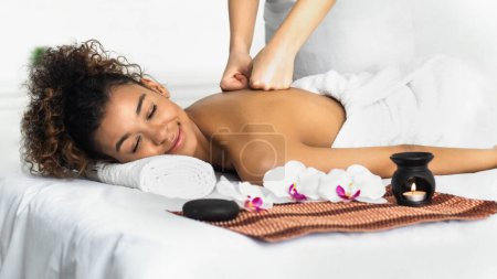 Téléchargez les photos : Massage d'arôme. Femme recevant un massage du dos dans un salon de spa, relaxant avec les yeux fermés - en image libre de droit