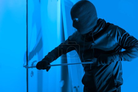 Un ladrón que intenta abrir una puerta con una palanca por la noche representa un escenario típico de allanamiento que representa una amenaza para la seguridad del apartamento.