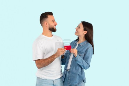 Two students, possibly a couple from generation z, standing close, sharing credit card, isolated on a blue background